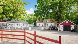 A rural property with a gravel riding arena, a stone building, a white house with a red barn, and a fenced area. - 4 bedroom beautiful home in Fleninge (Fleninge)