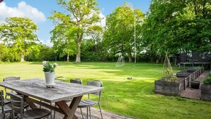 A wooden deck with a table and chairs, surrounded by a grassy lawn and trees. - 4 bedroom beautiful home in Fleninge (Fleninge)