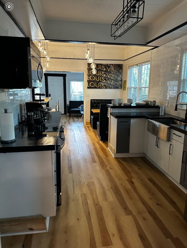 Una cocina moderna con una isla central, suelo de madera y una zona de comedor con sofá y mesa negros.