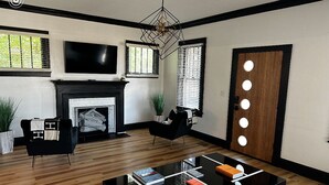 Una sala de estar moderna con chimenea, muebles negros, una mesa de centro de vidrio y un televisor montado en la pared.