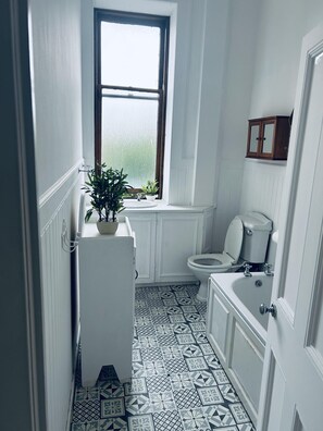 Ein schmales Badezimmer mit Fenster, Toilette, Waschbecken und Schrank.