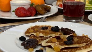 A breakfast setting with pancakes topped with berries and syrup, a glass of red juice, and a plate of oranges and strawberries. - Sym Hotel - Chéraga (Algiers)