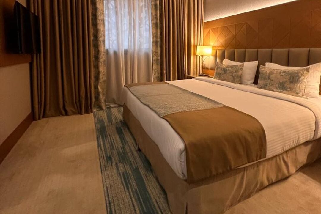 A hotel room with a large bed, a flat-screen TV mounted on the wall, and a window with curtains.