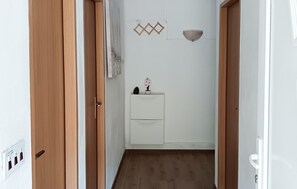 Um corredor estreito com portas de madeira, parede branca, um pequeno armário branco e uma prateleira fixada na parede.