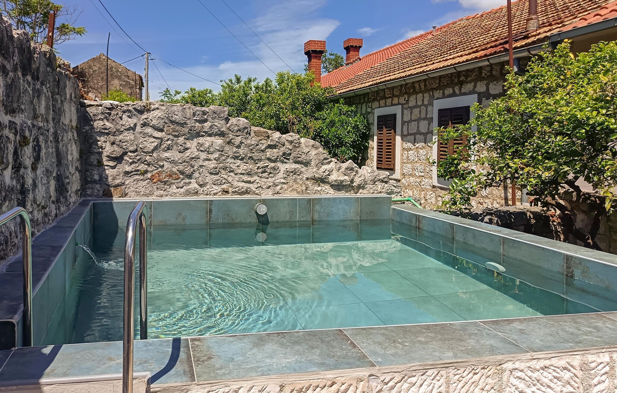 Una piscina con un muro de piedra y un edificio con techo de tejas al fondo.