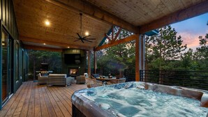 Een houten terras met een jacuzzi, tuinmeubilair en uitzicht op bomen.