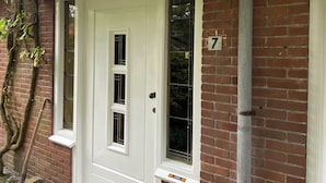 Une porte d’entrée blanche avec une petite fenêtre, un mur en briques et une plaque portant le numéro 7.