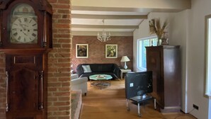 Un salon avec une cheminée en briques, un canapé noir, un lustre et un grand meuble en bois.