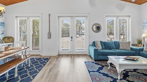 A spacious living room with a high ceiling, a blue sofa, a coffee table, and a dining area with a wooden bench and a patterned rug. - SEA-REST!! Relaxed 4br 4ba home, POOL and close to the BEACH! (Alys Beach)