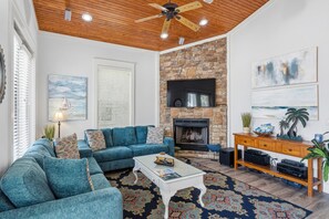 Un salon avec une cheminée en pierre, un canapé bleu, une table basse et un meuble de rangement en bois pour les appareils multimédias.