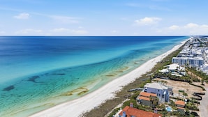 An aerial view of a coastal area with a beach, clear blue waters, and a row of buildings with a uniform architectural style. - SEA-REST!! Relaxed 4br 4ba home, POOL and close to the BEACH! (Alys Beach)