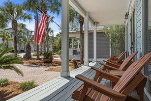 Une véranda couverte avec des chaises en bois, un drapeau et une maison dotée d’une véranda.