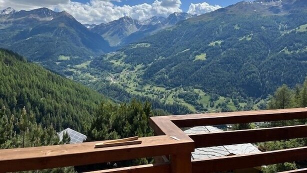 Paisaje montañoso con una terraza de madera y vistas al valle.