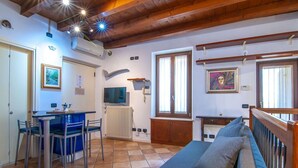 A cozy room with a wooden ceiling, a dining area with a table and chairs, a sofa, and a window with curtains.