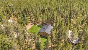 Une vue aérienne d’un chalet entouré d’une forêt dense, avec une pelouse bien entretenue et une grande terrasse.