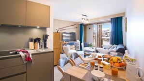 A modern kitchen with a dining area, a living room with a sofa and a view of the outside. - Ski aux pieds & piscine | T2 + cabine (Alpe d'Huez)