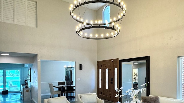 A spacious living room with a modern chandelier, white sofas, a glass coffee table, and a large mirror. - w/pool 5 min to the Strip (Las Vegas)