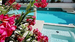 A swimming pool with clear blue water, surrounded by a white building and lush greenery. - w/pool 5 min to the Strip (Las Vegas)