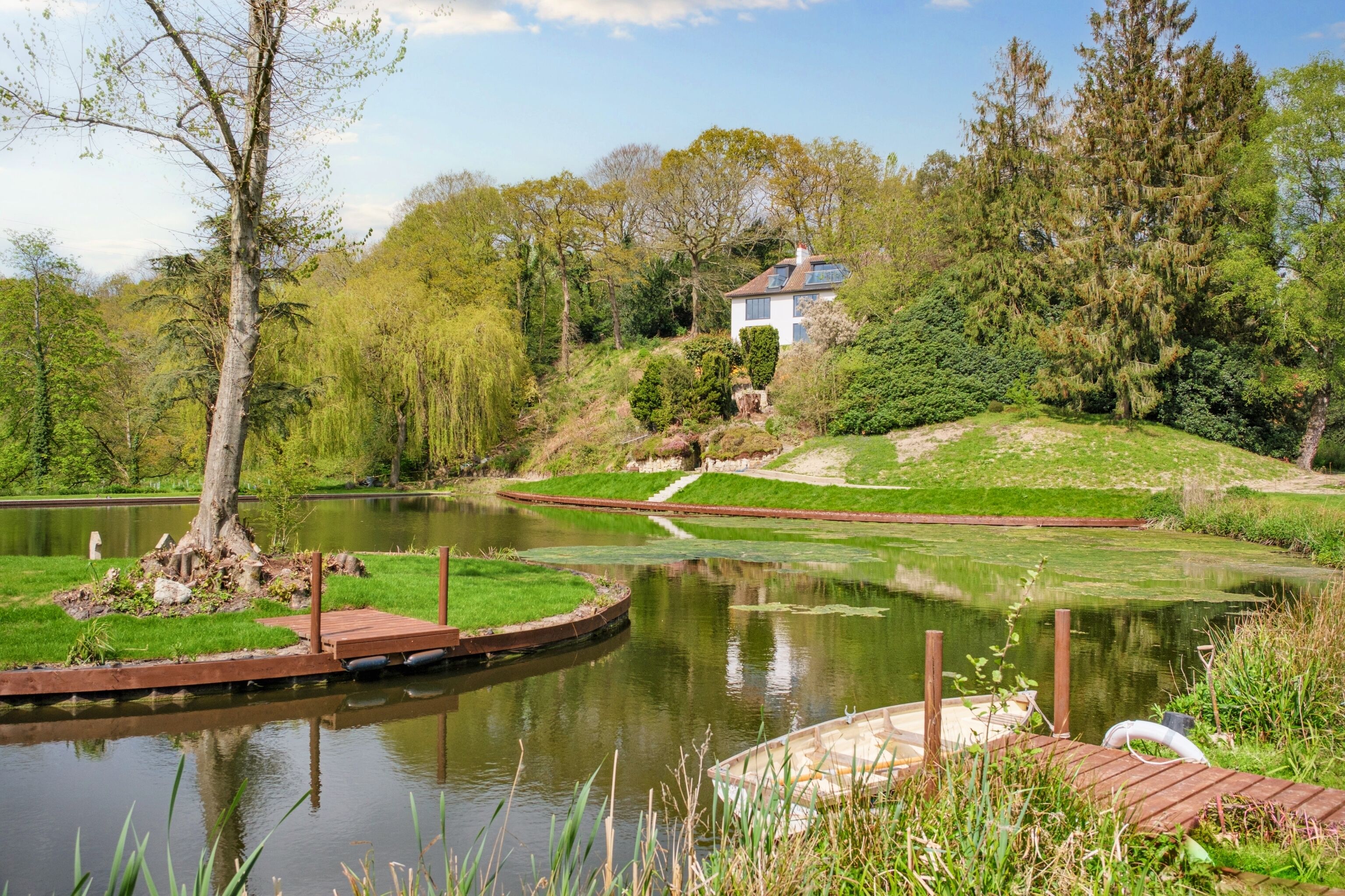 A serene lakeside setting with a wooden dock, a small boat, and a house nestled among lush greenery.