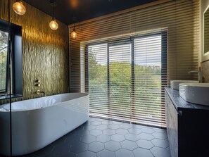 A modern bathroom with a large bathtub, wooden wall panels, and a view through large windows.