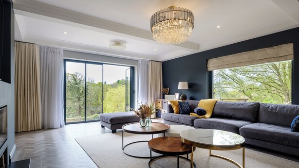 A modern living room with a grey sofa, two round coffee tables, a chandelier, and large windows with curtains. - 5 Bed Lake House - Sleeps 10 - Nature Reserve (Devizes)