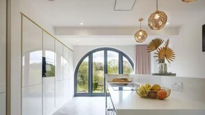 A modern kitchen with a large window, white cabinetry, and a central island with fruit. - 5 Bed Lake House - Sleeps 10 - Nature Reserve (Devizes)