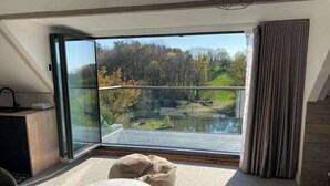 A modern room with a large glass door leading to a balcony with a view of a lake and trees. - 5 Bed Lake House - Sleeps 10 - Nature Reserve (Devizes)