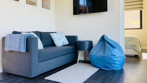 Ein modernes Wohnzimmer mit grauem Sofa, einem blauen Sitzsack, einem Flachbildfernseher und drei abstrakten Wandbildern.