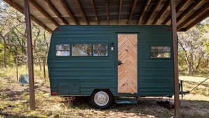 Un camping-car vert est garé sous un abri en bois dont la porte est ornée d’un motif en chevrons.