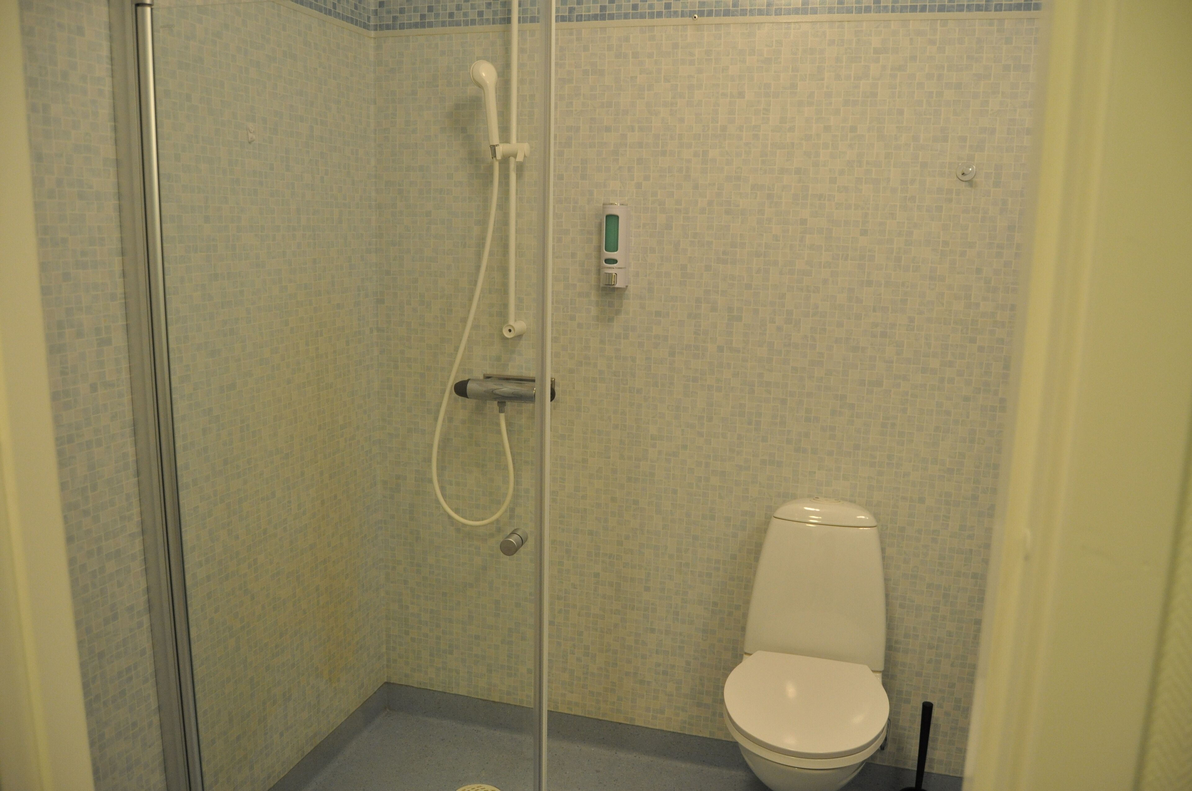 A bathroom with a shower, toilet, and a hand sanitizer dispenser.