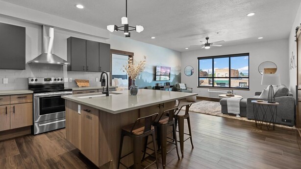 A modern kitchen with a large island, stainless steel appliances, and a dining area with a sofa and chairs. - Beautifully Designed, Fully Stocked New Condo with Custom Features - Plus A Gym! (Columbia Falls)