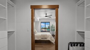 A bedroom with a bed, a ceiling fan, a window with a view, and a potted plant. - Beautifully Designed, Fully Stocked New Condo with Custom Features - Plus A Gym! (Columbia Falls)
