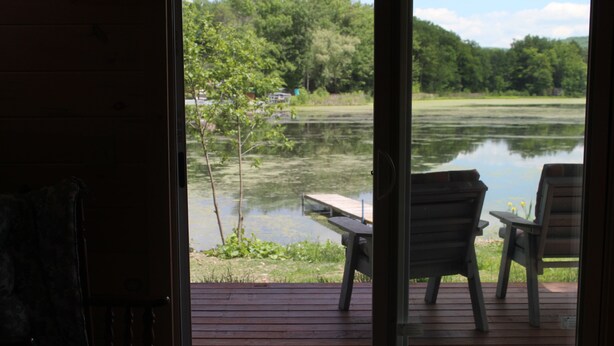 An open door leading to a deck with two chairs and a table overlooking a lake.