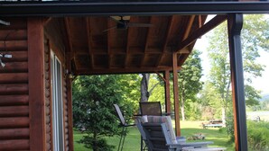 A wooden cabin with a covered porch, two chairs, a table, and a laptop.