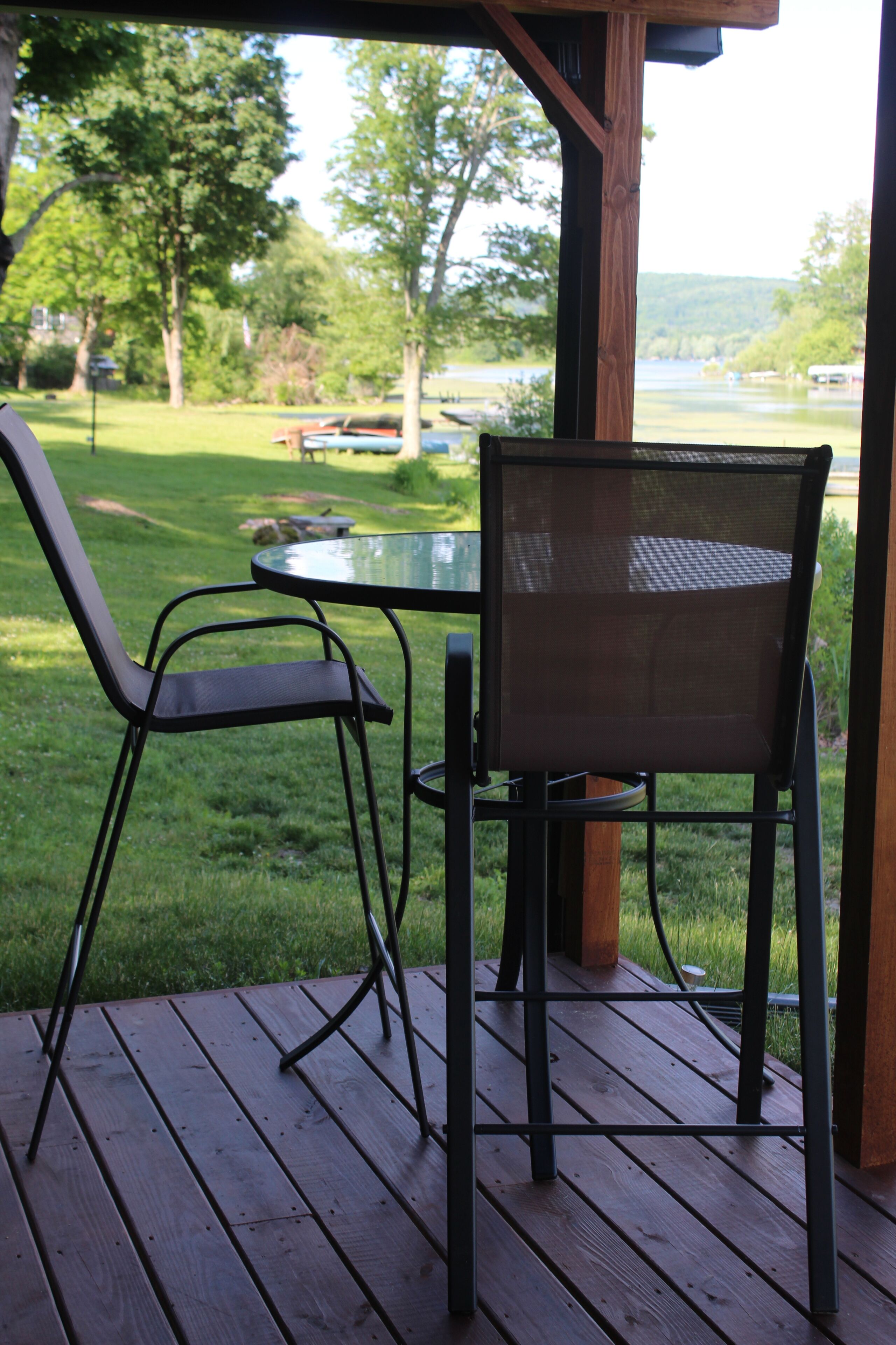 Une terrasse en bois avec une table et deux chaises, donnant sur une zone verdoyante avec des arbres et une étendue d’eau.