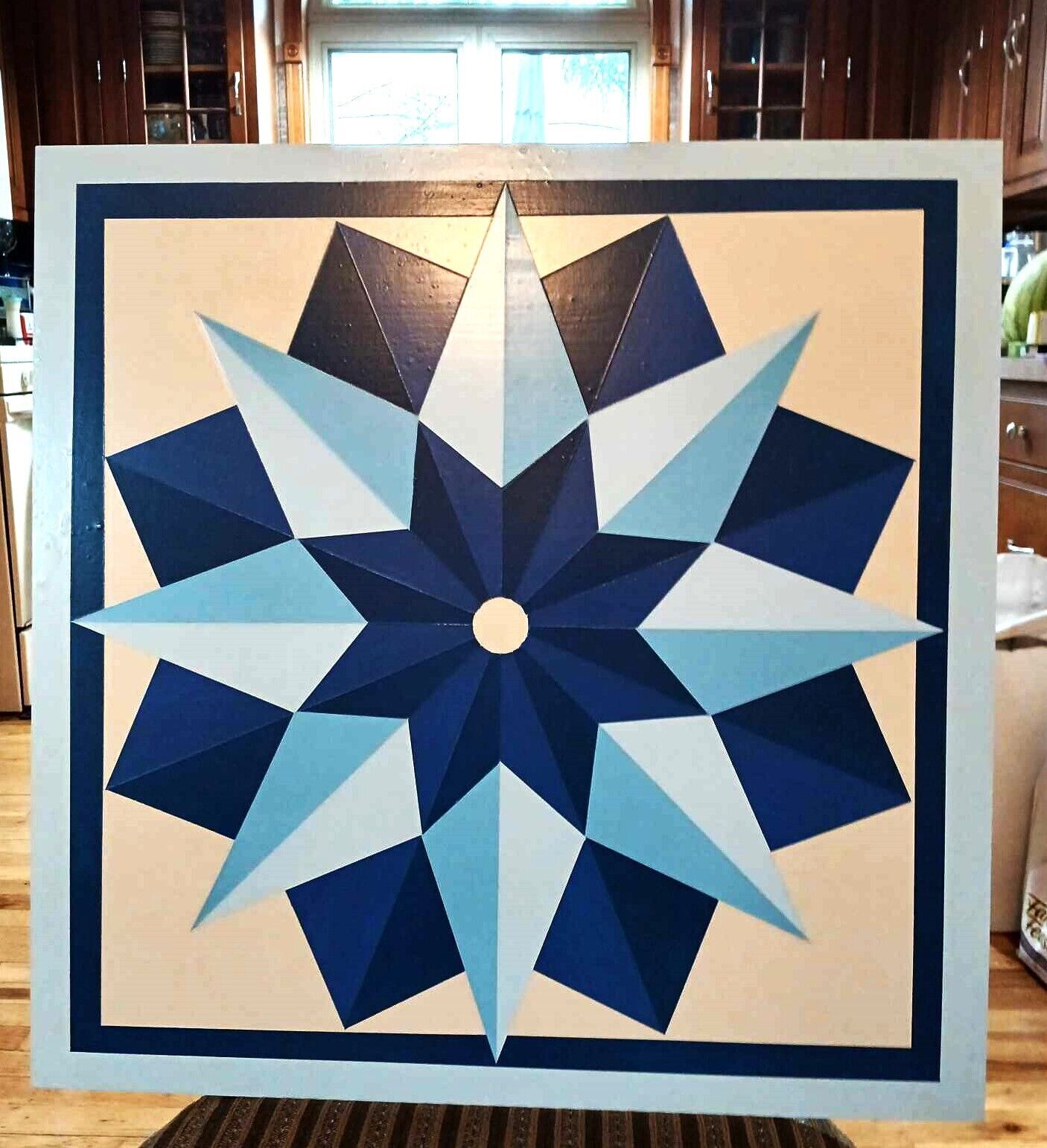 Una obra de arte geométrica enmarco, con un elemento circular central, rodeado por un diseño tipo estrella, sobre una superficie de madera.
