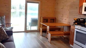 A cabin interior with a wooden ceiling, a sofa, a dining table, and a kitchen area including an oven.