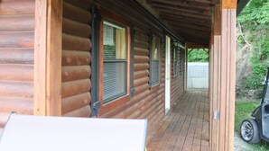 A log cabin with a covered porch, wooden exterior, and a vehicle parked outside.