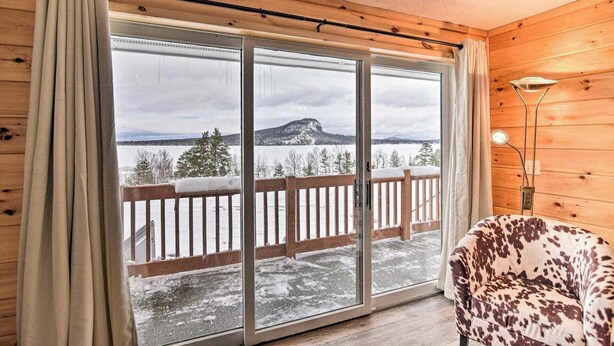A room with a large sliding glass door leading to a balcony with a wooden railing, a chair, and a lamp. - Kineo Overlook (Beautiful Mountain Views) (Rockwood)