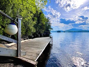 A wooden dock extending into calm water, surrounded by lush greenery and distant mountains.