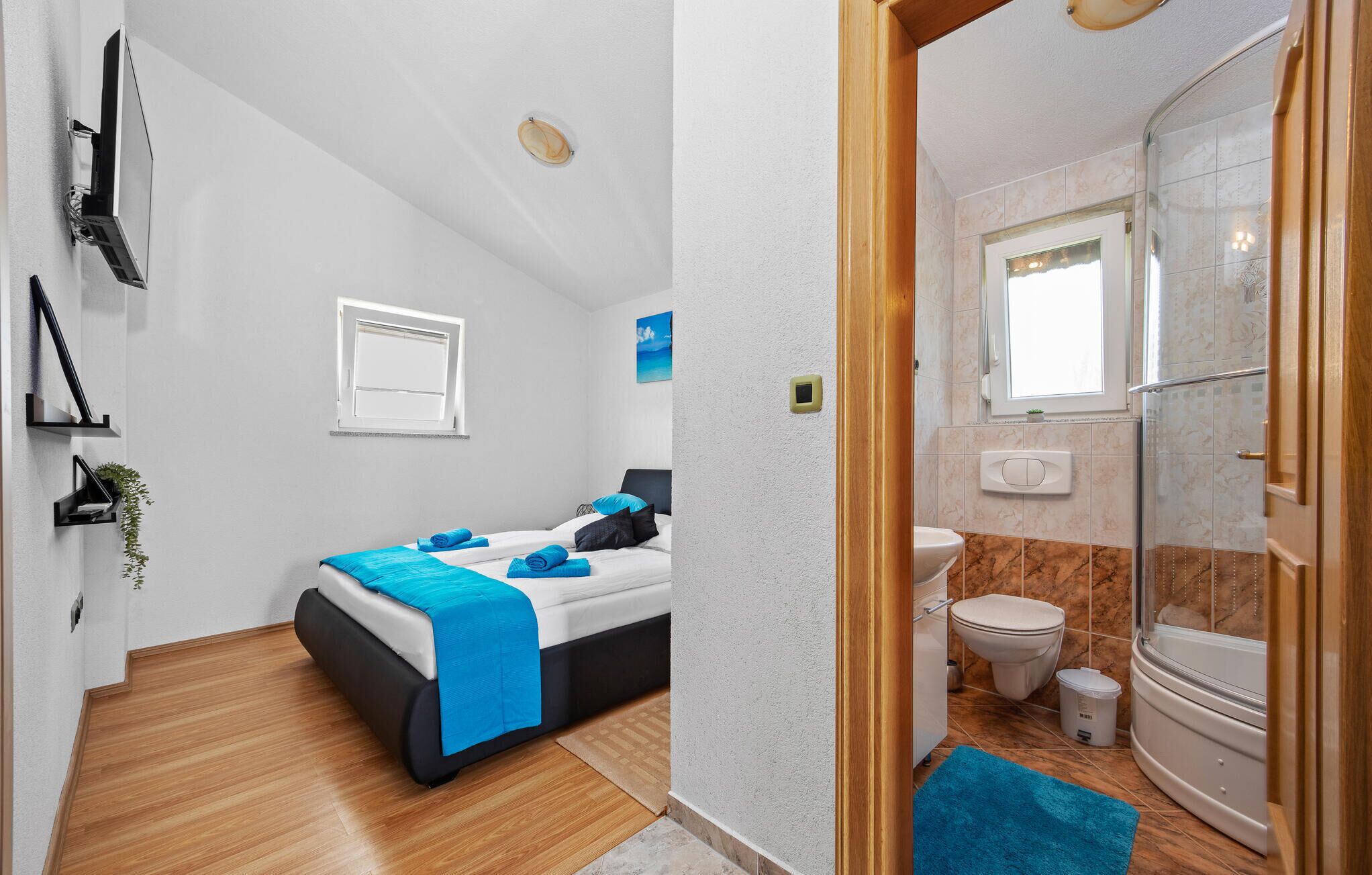 A hotel room with a bed, a window, a bathroom with a toilet and shower, and a small plant on the wall.