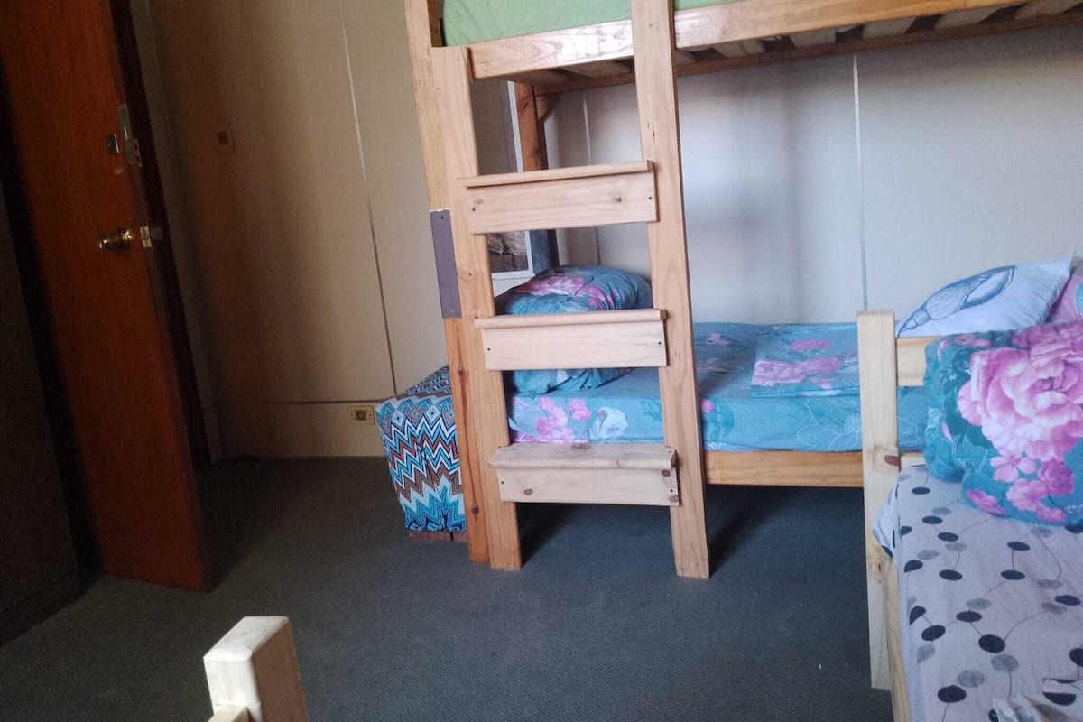 Quarto com beliche, escada de madeira, porta e piso coberto de carpete.