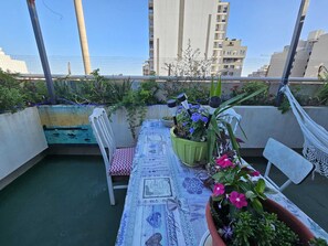 Eine Dachterrasse mit Tisch für zwei Personen, umgeben von Topfpflanzen und einer Hängematte.