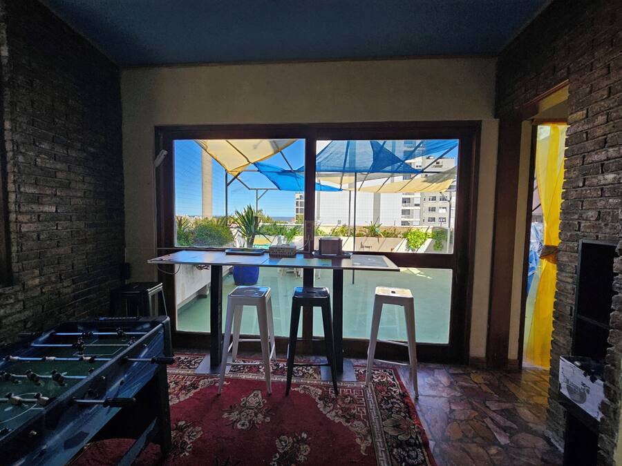 A room with a large window, a table with two stools, a foosball table, and a fireplace.