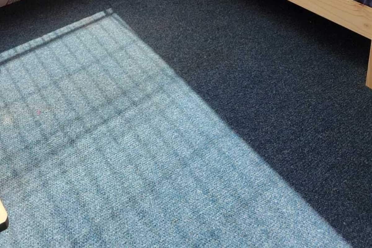 Uma cama beliche com escada, uma janela com cortinas e uma caixa no chão.
