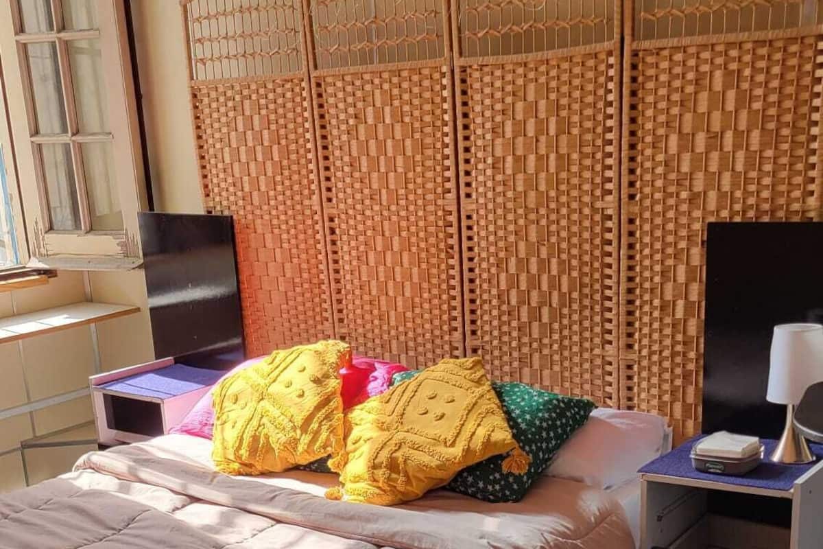 Quarto com cama, mesa de cabeceira, luminária e cabeceira em tecido.