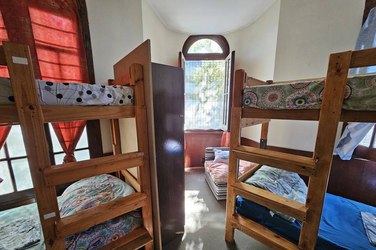 Quarto de dormitório com beliches, janela com cortinas e porta para outro quarto.
