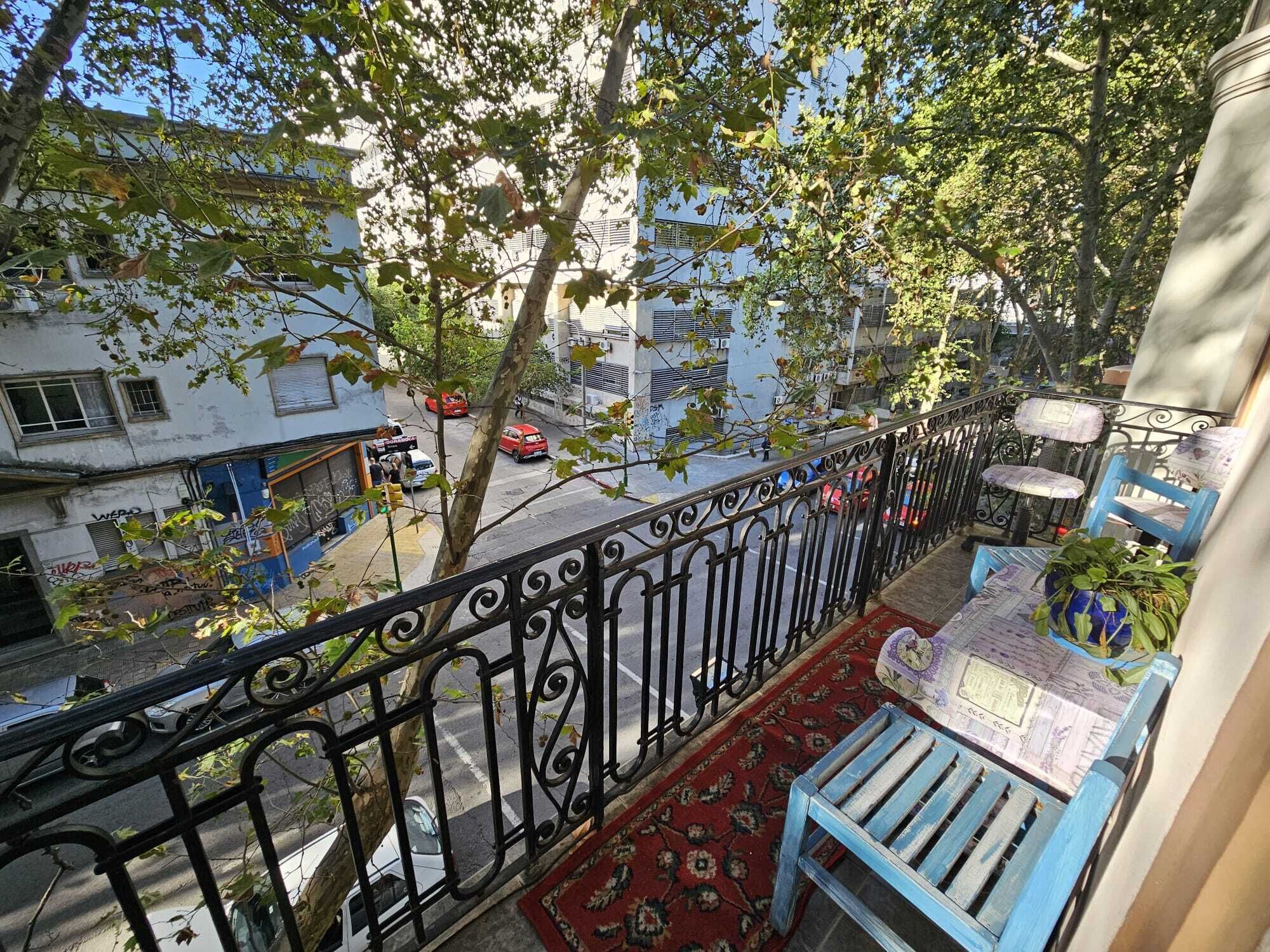 A balcony with a metal railing, a blue chair, a small table, and a potted plant.