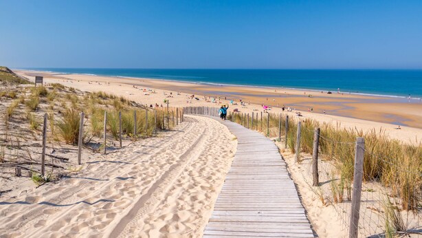Een zandstrand met een houten vogelzangpad dat naar het water loopt.