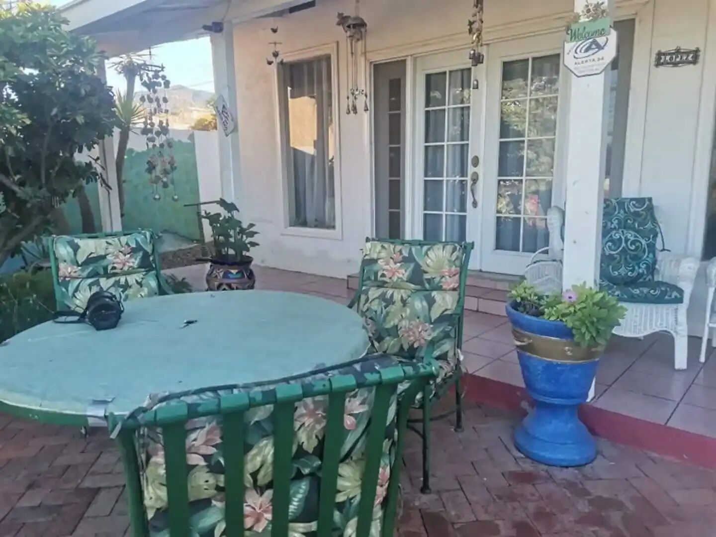 A patio with a round table and chairs, potted plants, and a white door with a sign.